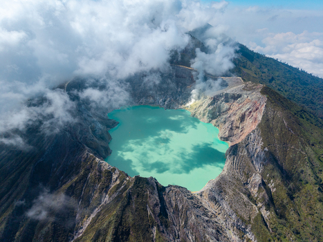 Aerial view of Ijen crater lake with its turquoise water surrounded by rugged volcanic slopes and clouds in Ijen East Java Indonesia.