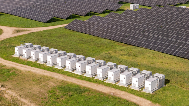Aerial view of a Battery Energy Storage System BESS facility with rows of white storage containers positioned next to a large solar farm in a grassy field in Poland. Aerial view of a Battery Energy Storage System BESS facility with rows of white storage containers positioned next to a large solar farm in a grassy field in Poland.