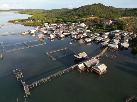 Aerial view of Galang Baru village featuring traditional houses on stilts and fish farm cages along the calm coastal waters in Galang Riau Islands Indonesia. Aerial view of Galang Baru village featuring traditional houses on stilts and fish farm cages along the calm coastal waters in Galang Riau Islands Indonesia.