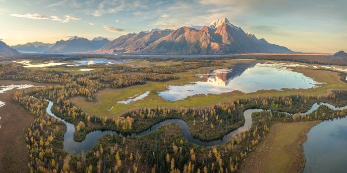 Aerial view of Chugach State Park featuring a winding river autumn forests and snow capped mountains under golden hour light Anchorage Alaska United States.