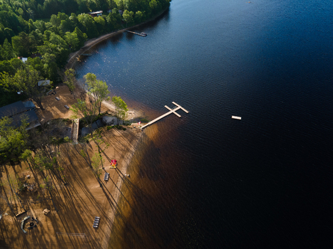 Aerial view of Commanda Lake featuring a wooden dock extending into the dark water a sandy shoreline and surrounding lush green forest in Restoule Ontario Canada. Aerial view of Commanda Lake featuring a wooden dock extending into the dark water a sandy shoreline and surrounding lush green forest in Restoule Ontario Canada.