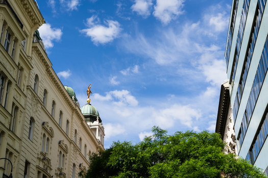 View of historic architecture with a green dome and golden statue alongside a modern glass building under a blue sky with wispy clouds Vienna Vienna Austria. View of historic architecture with a green dome and golden statue alongside a modern glass building under a blue sky with wispy clouds Vienna Vienna Austria.