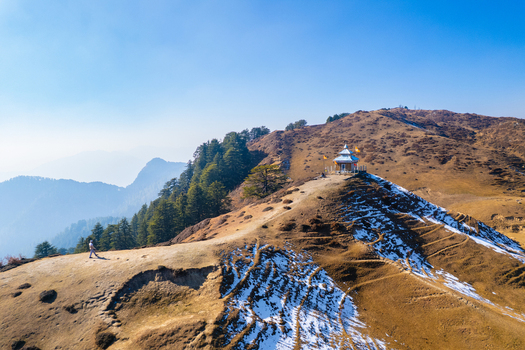 Aerial view of a small mountain temple on a ridge with a person walking along a path and snow covered slopes in Chakrata Uttarakhand India. Aerial view of a small mountain temple on a ridge with a person walking along a path and snow covered slopes in Chakrata Uttarakhand India.