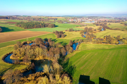 Aerial view of the winding Aisch river and Aischtalweg path surrounded by green meadows and forests near Uehlfeld Bayern Germany. Aerial view of the winding Aisch river and Aischtalweg path surrounded by green meadows and forests near Uehlfeld Bayern Germany.
