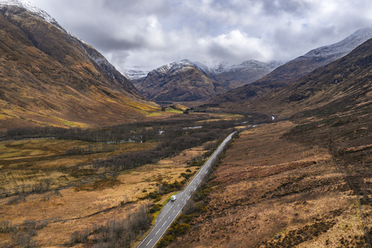 Aerial view of a winding road through a dramatic valley with snow capped mountains and a white campervan in Scotland United Kingdom. Aerial view of a winding road through a dramatic valley with snow capped mountains and a white campervan in Scotland United Kingdom.