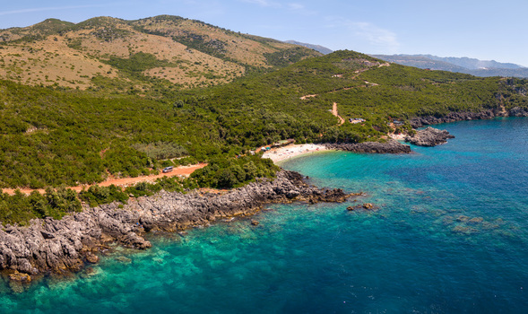 Aerial view of Aquarium Beach with its turquoise waters rocky shoreline and lush green hills in Jala Vlore County Albania.