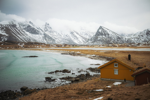 View of a yellow cabin standing out against the backdrop of snow covered mountains and turquoise sea a serene contrast in winter Fredvang Nordland Norway. View of a yellow cabin standing out against the backdrop of snow covered mountains and turquoise sea a serene contrast in winter Fredvang Nordland Norway.