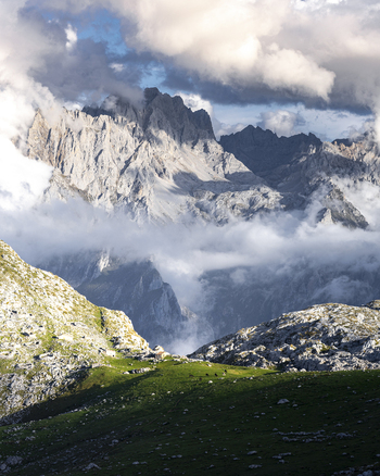 View of jagged peaks piercing through the swirling clouds with vibrant green meadows contrasting the rugged terrain Picos de Europa Asturias Spain. View of jagged peaks piercing through the swirling clouds with vibrant green meadows contrasting the rugged terrain Picos de Europa Asturias Spain.