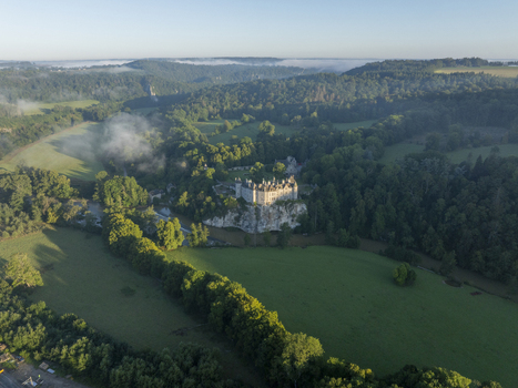 Aerial view of Chateau de Walzin perched on a cliff above the Lesse river surrounded by lush green forests and misty meadows in Dinant Region wallonne Belgium.
