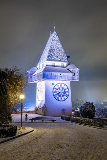 View of the illuminated clock tower standing majestically against the night sky its details dusted with snow glowing softly above the city Graz Styria Austria. View of the illuminated clock tower standing majestically against the night sky its details dusted with snow glowing softly above the city Graz Styria Austria.