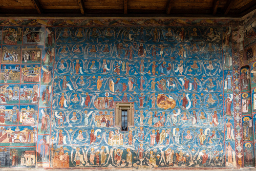 View of the intricate and vibrant blue exterior frescoes depicting religious scenes on the walls of the historic Voronet Monastery in Voronet Judetul Suceava Romania. View of the intricate and vibrant blue exterior frescoes depicting religious scenes on the walls of the historic Voronet Monastery in Voronet Judetul Suceava Romania.