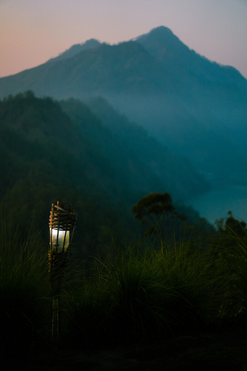View of a glowing bamboo torch set against the misty silhouette of Mount Batur at dusk in Kintamani Bali Indonesia.