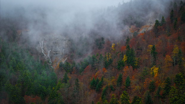 Aerial view of a misty mountain slope ablaze with autumnal hues punctuated by a delicate waterfall cascading down the rock face Gex Auvergne Rhône Alpes France. Aerial view of a misty mountain slope ablaze with autumnal hues punctuated by a delicate waterfall cascading down the rock face Gex Auvergne Rhône Alpes France.