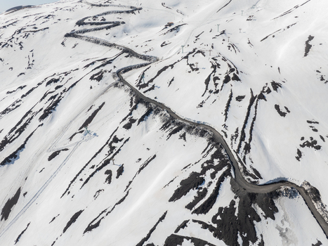 Aerial view of the winding mountain road on the snow covered south slope of Mount Etna with volcanic rock and ski lift pylons Nicolosi Sicilia Italy. Aerial view of the winding mountain road on the snow covered south slope of Mount Etna with volcanic rock and ski lift pylons Nicolosi Sicilia Italy.