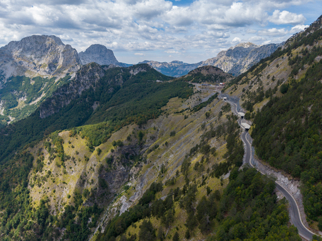 Aerial view of the Albanian Alps featuring a winding mountain road with tunnels cutting through rugged green slopes and rocky peaks in Shkoder Shkoder County Albania. Aerial view of the Albanian Alps featuring a winding mountain road with tunnels cutting through rugged green slopes and rocky peaks in Shkoder Shkoder County Albania.