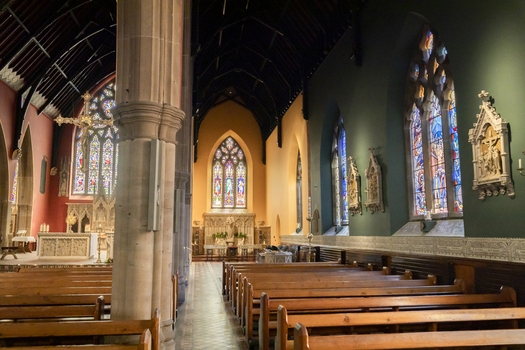 View of the interior of St. Mary s Cathedral with wooden pews stone columns and colorful stained glass windows in Newcastle upon Tyne England United Kingdom. View of the interior of St. Mary s Cathedral with wooden pews stone columns and colorful stained glass windows in Newcastle upon Tyne England United Kingdom.