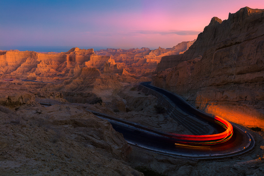 View of Makran Coastal Highway winding through the rugged desert mountains of Buzi Top pass with light trails from a vehicle at dusk in Balochistan Pakistan.