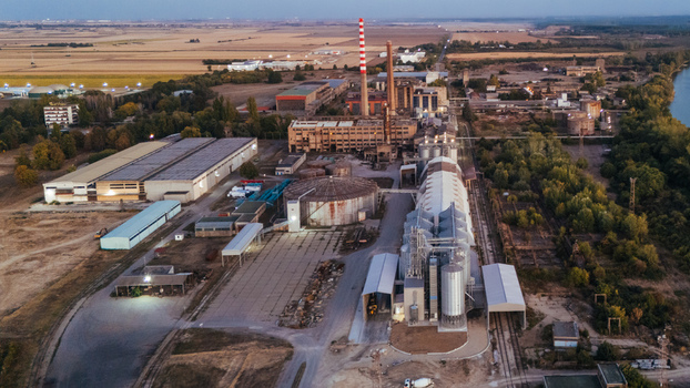 Aerial view of an industrial facility with tall chimneys grain silos and warehouses situated near a river and agricultural fields in Sremska Mitrovica Vojvodina Serbia.