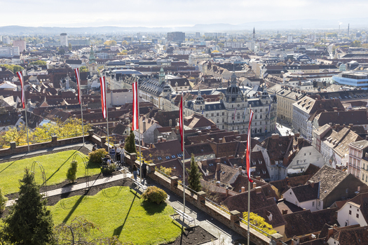 View of red flags fluttering above the terracotta rooftops a green lawn and the cityscape stretching to the horizon Graz Styria Austria. View of red flags fluttering above the terracotta rooftops a green lawn and the cityscape stretching to the horizon Graz Styria Austria.