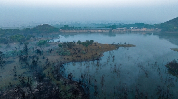 Aerial view of the serene lake surrounded by sparse vegetation and misty hills at dawn in Jodhpur Rajasthan India. Aerial view of the serene lake surrounded by sparse vegetation and misty hills at dawn in Jodhpur Rajasthan India.