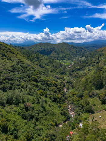 Aerial view of Bomburu Ella Waterfall surrounded by lush green hills and dense tropical forest under a bright blue sky in Nuwara Eliya Central Province Sri Lanka. Aerial view of Bomburu Ella Waterfall surrounded by lush green hills and dense tropical forest under a bright blue sky in Nuwara Eliya Central Province Sri Lanka.