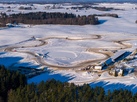 Aerial view of a winding ice racing track with cars surrounded by snow covered fields and dense evergreen forests in Moletai Utena County Lithuania.