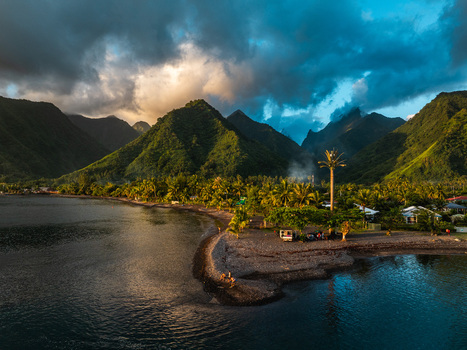 Aerial view of lush tropical mountains rising above a volcanic beach and turquoise lagoon under a dramatic sunset sky Moorea Maiao Windward Islands French Polynesia. Aerial view of lush tropical mountains rising above a volcanic beach and turquoise lagoon under a dramatic sunset sky Moorea Maiao Windward Islands French Polynesia.