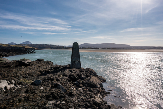 Aerial view of Ballyness Bay featuring a stone marker on a rocky seaweed covered shoreline with distant hills under a bright sky in Ballyness County Donegal Ireland. Aerial view of Ballyness Bay featuring a stone marker on a rocky seaweed covered shoreline with distant hills under a bright sky in Ballyness County Donegal Ireland.