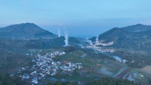Aerial view of the Dieng Plateau featuring the village of Kejajar surrounded by volcanic mountains and geothermal steam plumes under a twilight sky in Kejajar Central Java Indonesia. Aerial view of the Dieng Plateau featuring the village of Kejajar surrounded by volcanic mountains and geothermal steam plumes under a twilight sky in Kejajar Central Java Indonesia.