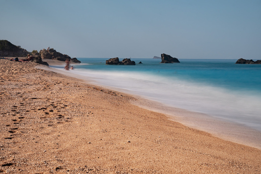 View of serene Kathisma Beach where golden sands meet the turquoise sea under a clear sky rocks dot the coastline Lefkada Greece. View of serene Kathisma Beach where golden sands meet the turquoise sea under a clear sky rocks dot the coastline Lefkada Greece.