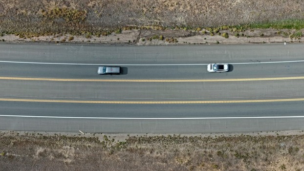 Aerial view of two cars driving on a multi lane highway surrounded by dry grassy fields in Golden Colorado United States.