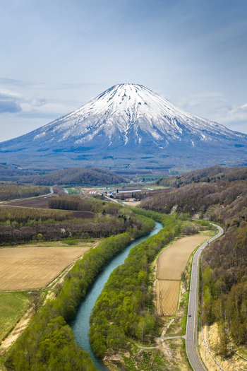 Aerial view of Mount Yotei with its snow capped peak rising above the lush green forests winding river and agricultural fields near Niseko Hokkaido Japan.