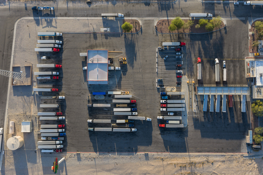 Aerial view of semi trucks parked in a large logistics lot with asphalt paving and surrounding desert landscape Enterprise Nevada United States. Aerial view of semi trucks parked in a large logistics lot with asphalt paving and surrounding desert landscape Enterprise Nevada United States.