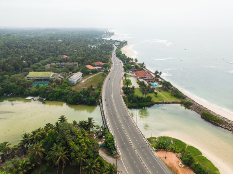 Aerial view of a coastal road winding between a lush tropical forest and a sandy beach along the Indian Ocean Koggala Southern Province Sri Lanka. Aerial view of a coastal road winding between a lush tropical forest and a sandy beach along the Indian Ocean Koggala Southern Province Sri Lanka.