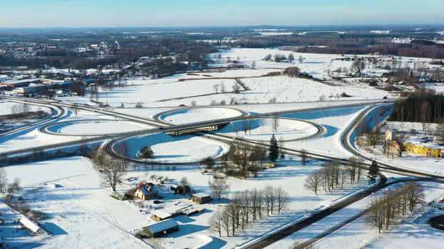 Aerial view of a cloverleaf interchange surrounded by snow covered fields trees and rural buildings in Latvia. Aerial view of a cloverleaf interchange surrounded by snow covered fields trees and rural buildings in Latvia.