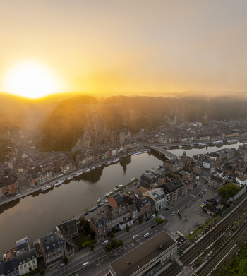 Aerial view of the Collegiate Church of Notre Dame de Dinant and the Meuse River at sunset with historic buildings and misty hills in Dinant Wallonia Belgium. Aerial view of the Collegiate Church of Notre Dame de Dinant and the Meuse River at sunset with historic buildings and misty hills in Dinant Wallonia Belgium.