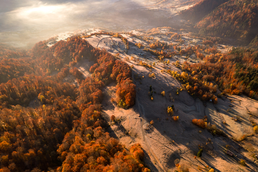 Aerial view of the autumn landscape with vibrant orange and yellow trees rolling hills covered in white frost and morning mist in the valley in Kvasy Zakarpattia Oblast Ukraine. Aerial view of the autumn landscape with vibrant orange and yellow trees rolling hills covered in white frost and morning mist in the valley in Kvasy Zakarpattia Oblast Ukraine.