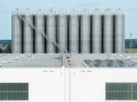 Aerial view of large cylindrical metallic storage tanks for petrochemical products situated behind a modern industrial building with solar panels on the roof in Poland.