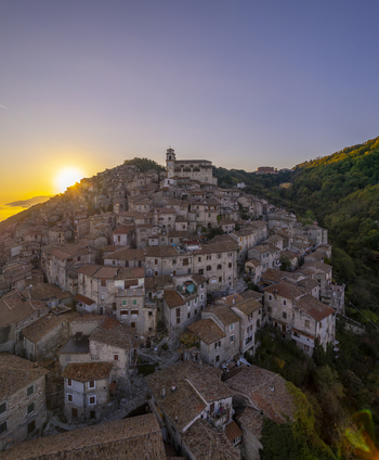 Aerial view of the historic hilltop town of Artena with stone houses terracotta rooftops and a church tower illuminated by the warm golden hour light in Artena Lazio Italy.