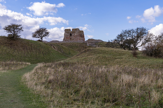 View of the historic ruins of Kalo Castle situated on a grassy hill under a blue sky with scattered clouds surrounded by rolling terrain and trees in Ronde Jutland Denmark. View of the historic ruins of Kalo Castle situated on a grassy hill under a blue sky with scattered clouds surrounded by rolling terrain and trees in Ronde Jutland Denmark.