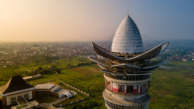 Aerial view of Menara Pandang Teratai tower with its lotus shaped top overlooking green fields and the city skyline during golden hour in Kecamatan Purwokerto Timur Jawa Tengah Indonesia. Aerial view of Menara Pandang Teratai tower with its lotus shaped top overlooking green fields and the city skyline during golden hour in Kecamatan Purwokerto Timur Jawa Tengah Indonesia.
