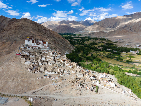 Aerial view of Thiksey Monastery perched on a hillside with traditional white buildings surrounded by arid mountains and green fields in Ladakh India. Aerial view of Thiksey Monastery perched on a hillside with traditional white buildings surrounded by arid mountains and green fields in Ladakh India.