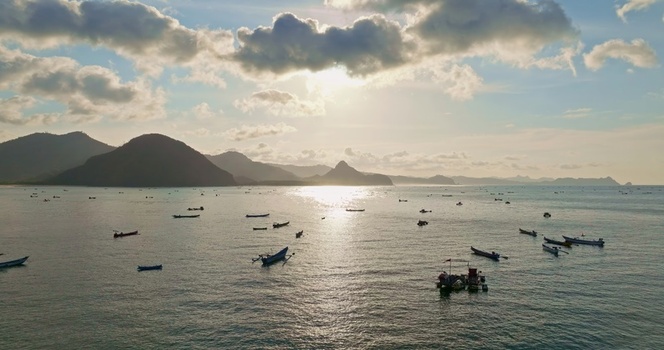 Aerial view of numerous traditional fishing boats scattered across a calm bay at sunset with mountains in the background in Lombok West Nusa Tenggara Indonesia.