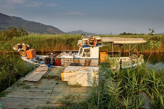 View of a small fishing boat docked at a wooden pier surrounded by tall reeds and mountains in the calm river of Akyaka Mugla Turkey. View of a small fishing boat docked at a wooden pier surrounded by tall reeds and mountains in the calm river of Akyaka Mugla Turkey.
