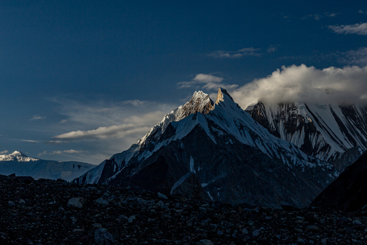 View of the dramatic snow capped peaks of the Karakoram range at the Concordia campsite featuring rugged rocky terrain and clouds in Concordia Gilgit Baltistan Pakistan.