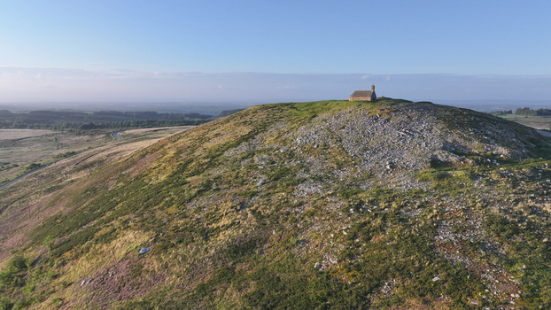 Aerial view of Chapelle Saint Michel de Brasparts sitting atop a rocky green hill under a clear blue sky in Saint Rivoal Bretagne France. Aerial view of Chapelle Saint Michel de Brasparts sitting atop a rocky green hill under a clear blue sky in Saint Rivoal Bretagne France.
