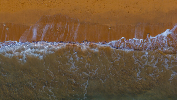 Aerial view of the sandy coastline and gentle waves washing onto the shore at West Bay England United Kingdom. Aerial view of the sandy coastline and gentle waves washing onto the shore at West Bay England United Kingdom.