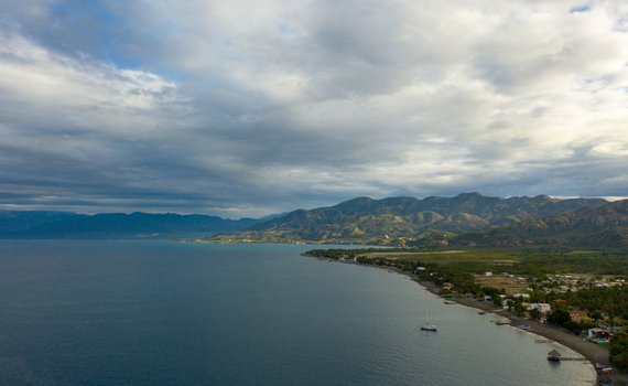 Aerial view of Palmar de Ocoa along the coast with calm bay waters small boats and lush mountains under a cloudy sky in Palmar de Ocoa Azua Province Dominican Republic.