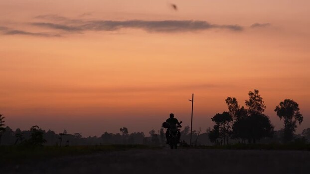 View of a motorcyclist riding on a rural road at sunset Bangladesh. View of a motorcyclist riding on a rural road at sunset Bangladesh.