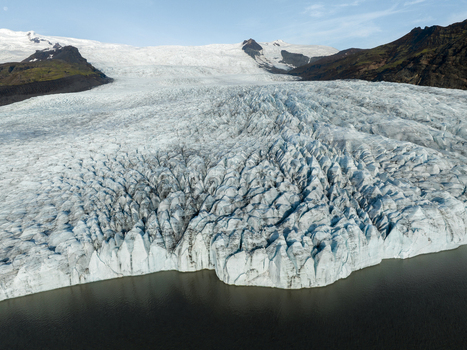 Aerial view of the glacial ice with its textured surface flowing into the dark waters contrasted against the backdrop of rugged mountains Fjallsarlon Sveitarfélagið Hornafjörður Iceland. Aerial view of the glacial ice with its textured surface flowing into the dark waters contrasted against the backdrop of rugged mountains Fjallsarlon Sveitarfélagið Hornafjörður Iceland.